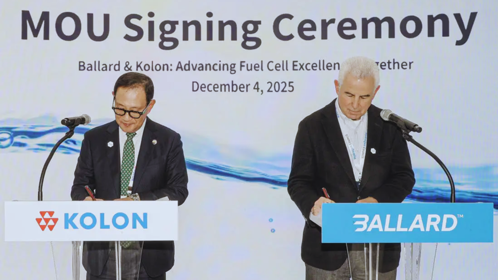 Ballard CEO Marty Neese and Kolon Industries President Sung Huh stand on stage signing MOU documentation