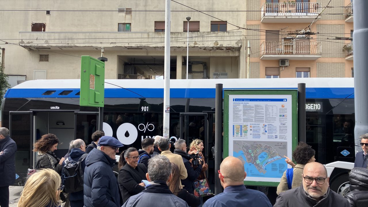 Passengers queue to board a blue and white public transit bus in Cagliari